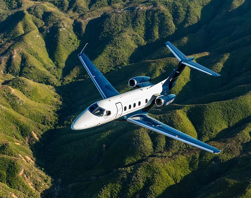 Geschäftsreisejet Embraer Phenom 300EV im Flug über grünen Hügeln, ausgerüstet mit Garmin Autoland