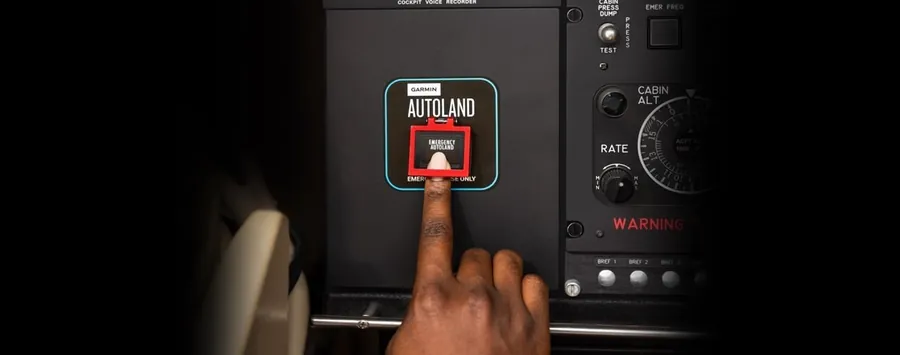Ein Finger drückt den roten Garmin-Autoland-Knopf im Cockpit eines Flugzeugs